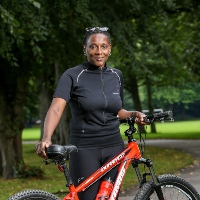 Carol Hutchinson, new to cycling, posing with her bike in the middle of a park in Greater Manchester