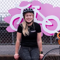 Lydia McGinely, a teacher in Perth, smiles as she sits on a wall wearing her helmet in front of a colourful cycling sign
