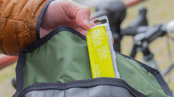 A small bright yellow puncture repair kit being taken out of a wallet. A bike is in the background.