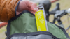A small bright yellow puncture repair kit being taken out of a wallet. A bike is in the background.