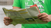 A close up of a regional map in a man's hands. The map is open and a route can be glimpsed. The background is his bright green t-shirt.