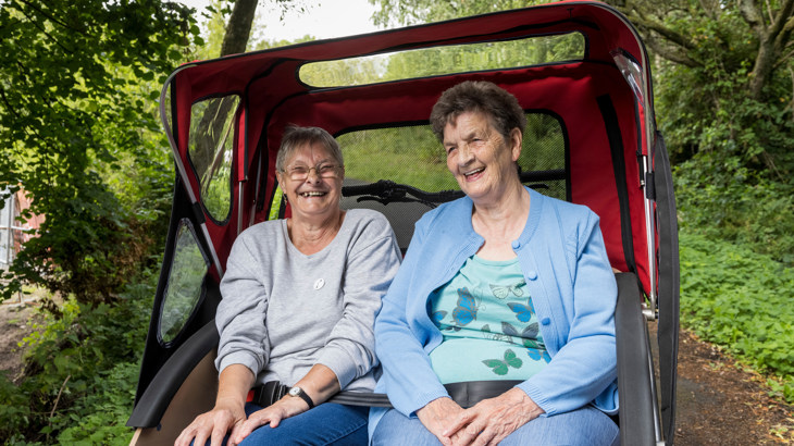 Two members of the Forever Young group pictured smiling as they sit aboard a trishaw