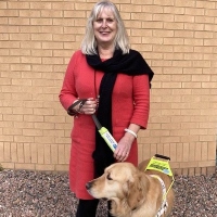 June from County Down smiling and standing with her guide dog Clyde