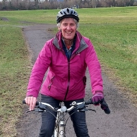 Karen Wilson smiling as she cycles on her bicycle through a park in Edinburgh
