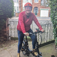 A young woman wearing a bright pink jumper stood outside her home in Manchester on her electric, folding bike