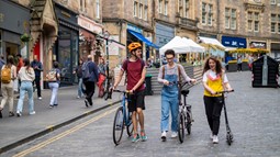 Three people walking alongside their bikes and scooters in the centre of Edinburgh on a pedestrianised street