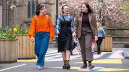 Three women walk along a street with brightly coloured artwork visible on the ground at Union Street, Dundee.