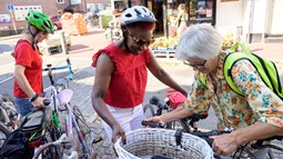 Three older women stood by their bikes, two are adjusting a basket that sits on the front of one of the bikes