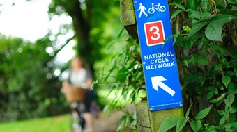 Blue and red sign for National Cycle Network Route 3 with cyclist in background