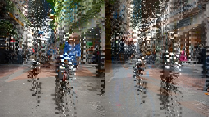 Two women riding bikes through a town centre