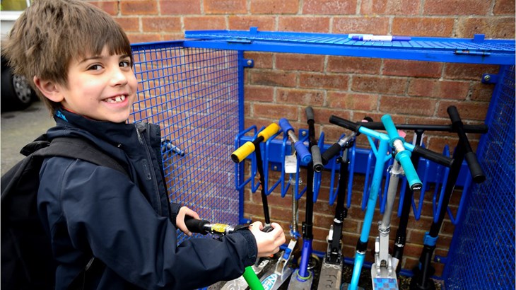 Boy smiling as he locks his scooter up at a stand in the school playground