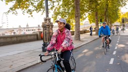 A girl cycles along a segregated cycle lane during the autumn time through Embankment in London, with other people cycling behind her in the background.