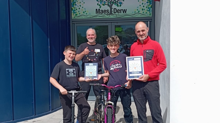 Sustrans staff member stands posing for a photo with staff and pupils from Maes Derw pupil referral unit after they achieved their Silver Active Travel School Award.